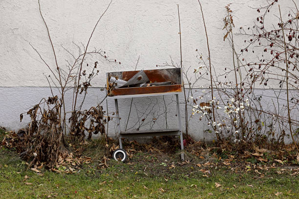 Broken grill on house wall between dry scrub and grass